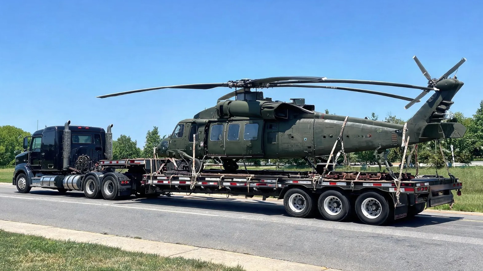 Military freight transportation — flatbed truck hauling military helicopter for DOD cargo delivery
